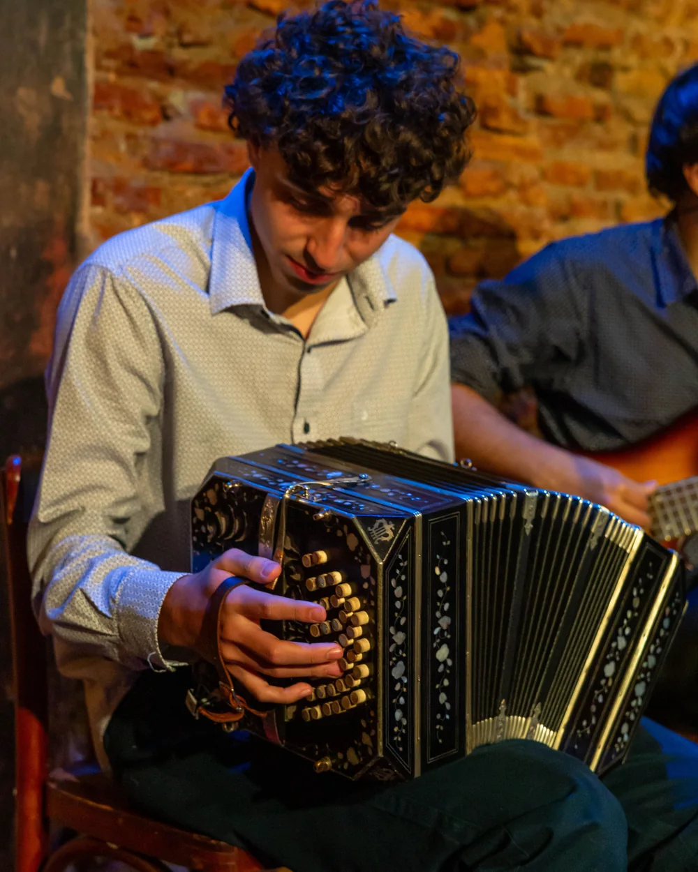En ung musiker, der spiller bandoneón i Argentina, en anden musiker ved hans side (repræsentativt fotografi af et rioplatensisk tangoorkester, ikke Primuseums egen trio)