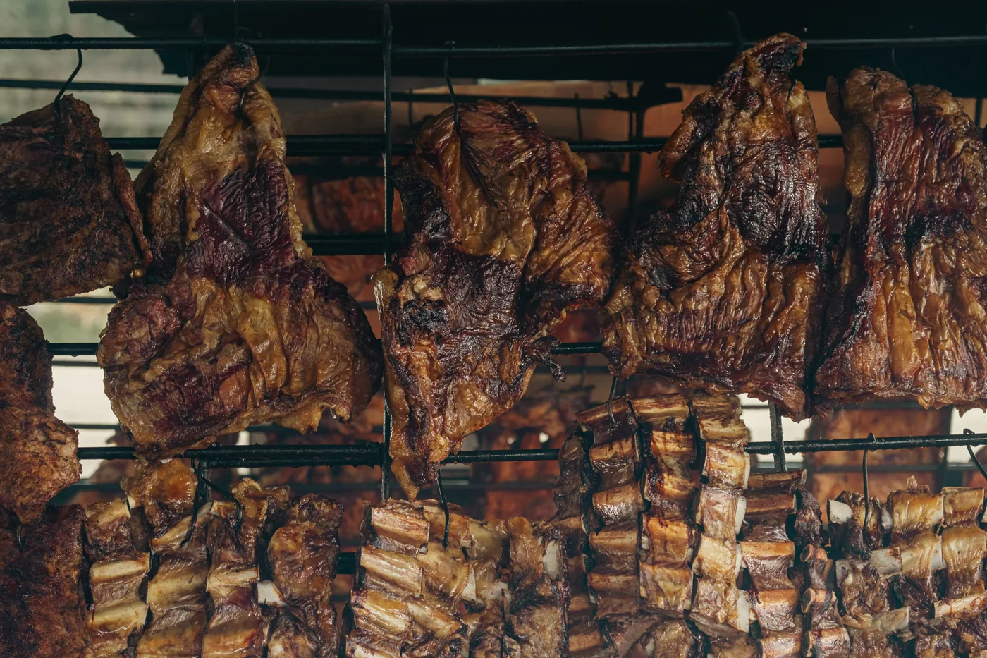 Cuts of grilled meat hanging over an open-fire parrilla grill (representative photograph of the Uruguayan/Argentine asado tradition, not Primuseum's own kitchen)